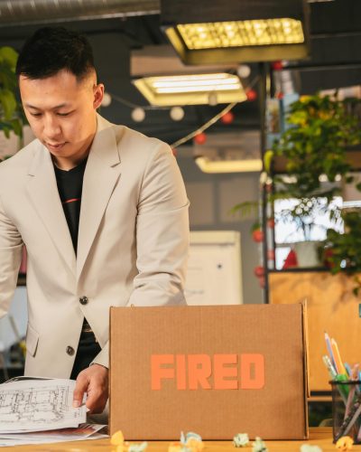Un employé range des documents dans une boîte étiquetée "LICENCIÉ" dans un environnement de bureau.