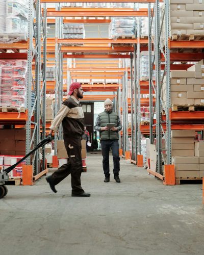 Deux travailleurs gèrent l'inventaire dans une grande allée d'entrepôt.