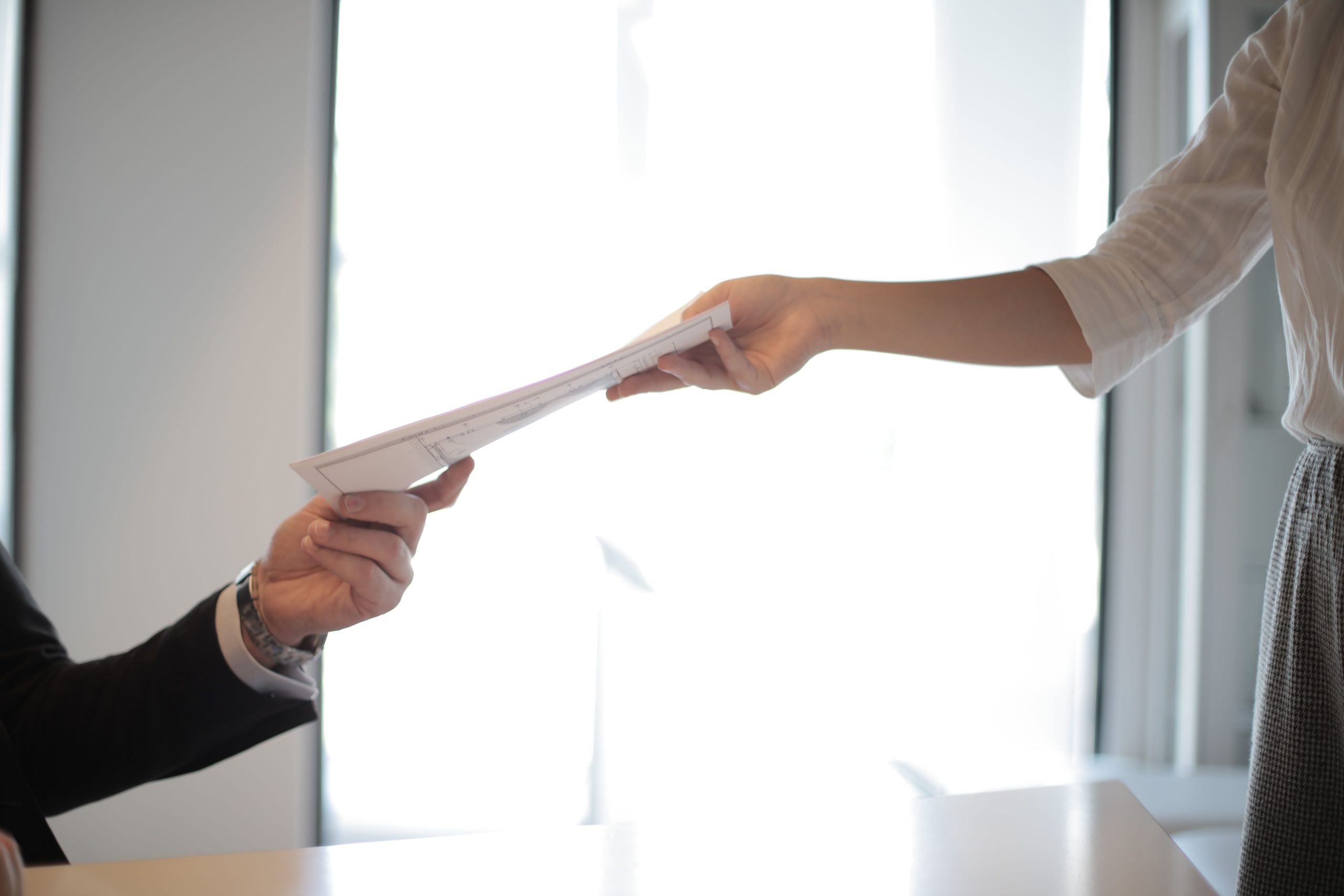 Close-up of hands exchanging documents in a business setting indoors. Gros plan sur des mains échangeant des documents dans un environnement professionnel intérieur.