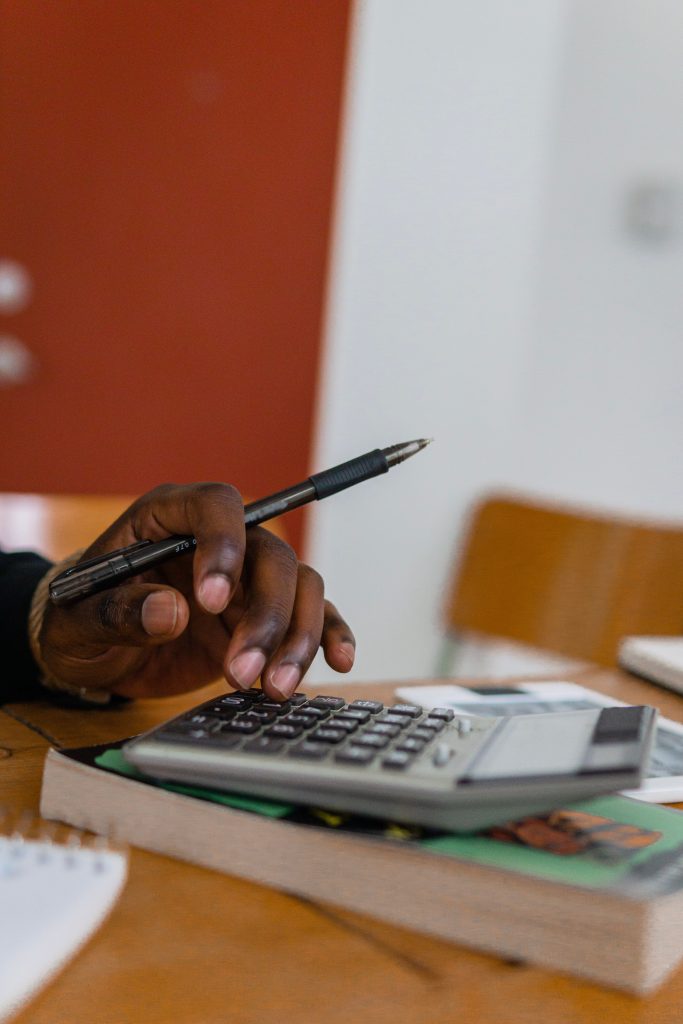 Close-up shot of a hand holding a pen while calculating finances with a calculator on a table. Gros plan sur une main tenant un stylo tout en calculant les finances avec une calculatrice sur une table.