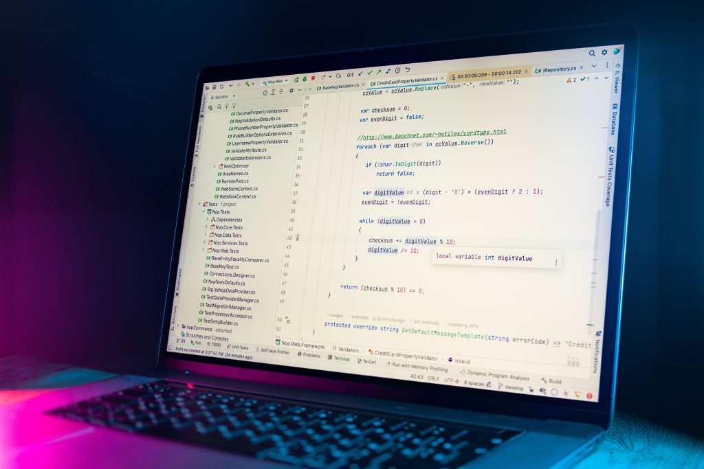 A laptop screen showing a code editor with visible programming code in a dimly lit environment. Un écran d'ordinateur portable affichant un éditeur de code avec du code de programmation visible dans un environnement faiblement éclairé.