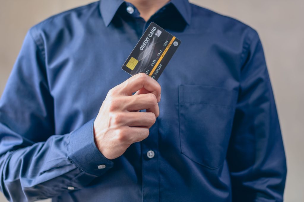 Close-up of a man in a blue shirt holding a credit card, symbolizing finance and security. Gros plan d'un homme en chemise bleue tenant une carte de crédit, symbolisant la finance et la sécurité.
