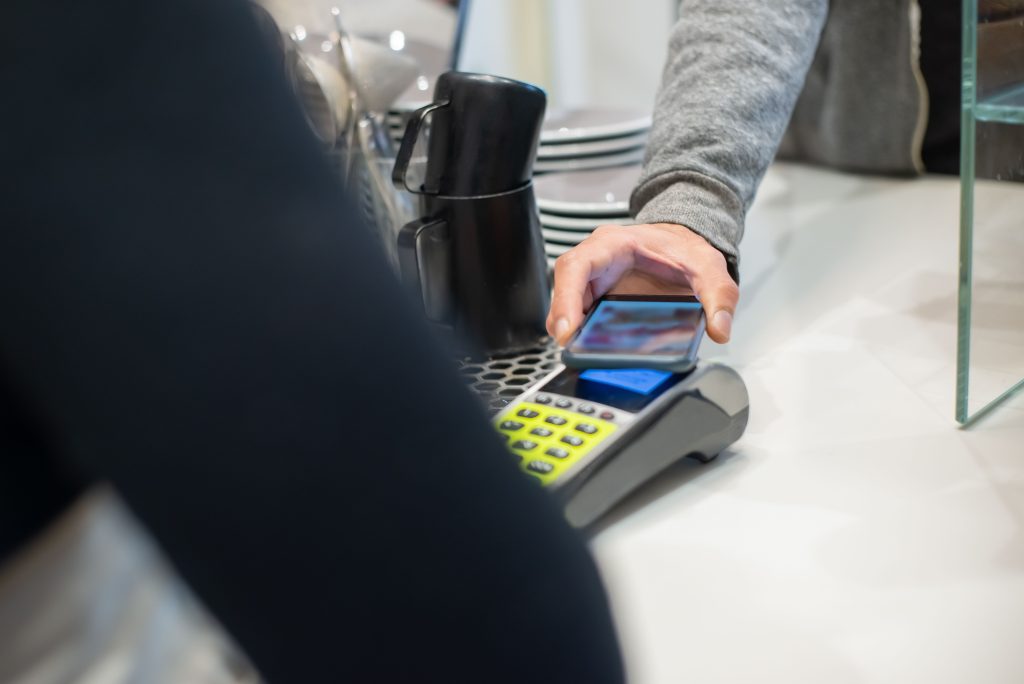 A customer makes a contactless payment using a smartphone at a café, showcasing modern digital transactions. Un client effectue un paiement sans contact à l'aide d'un smartphone dans un café, mettant en avant les transactions numériques modernes.