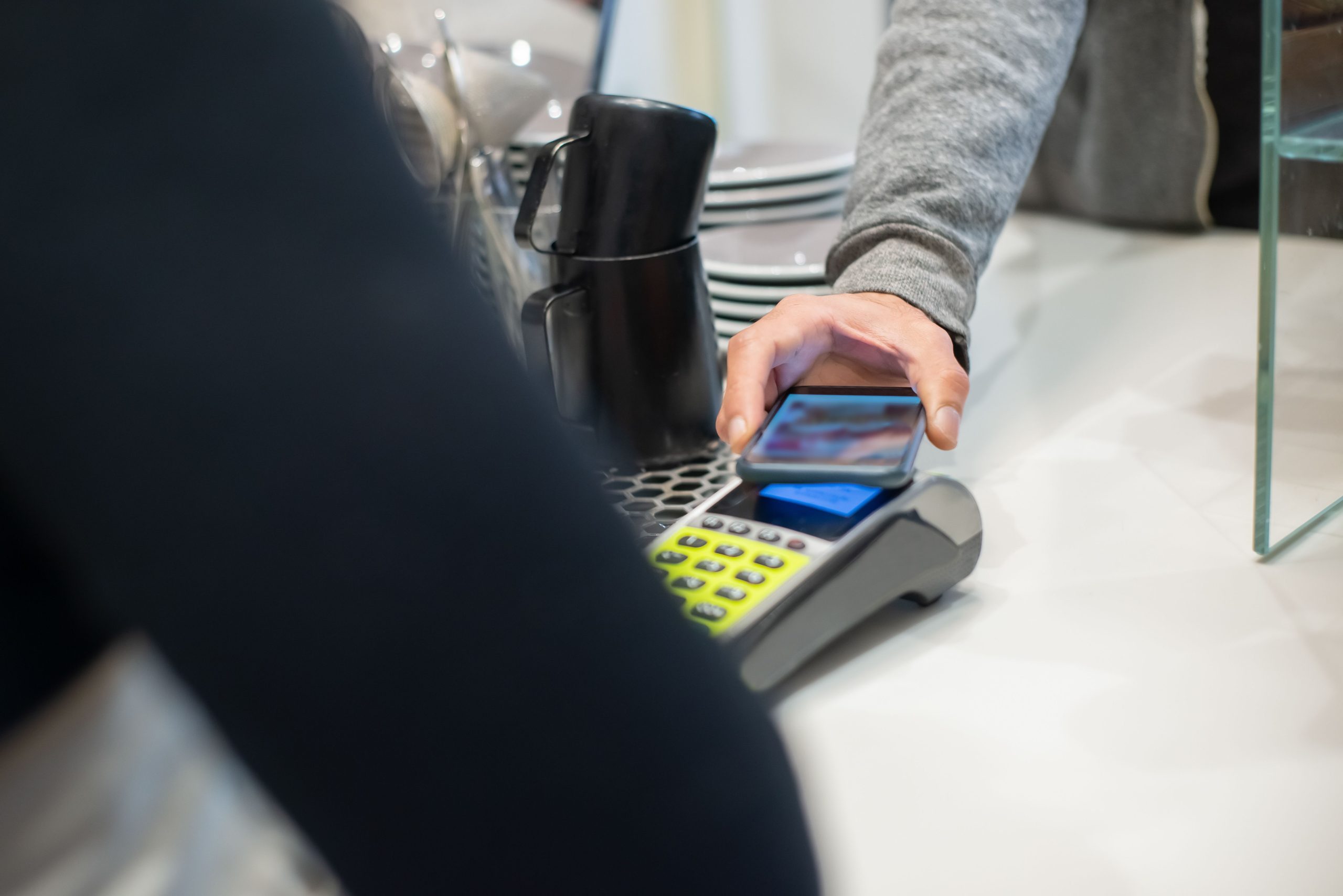 A customer makes a contactless payment using a smartphone at a café, showcasing modern digital transactions. Un client effectue un paiement sans contact à l'aide d'un smartphone dans un café, mettant en avant les transactions numériques modernes.