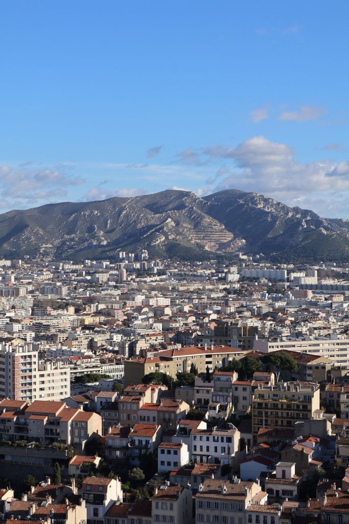 A breathtaking aerial view showcasing Marseille's cityscape with mountains in the background under a clear sky. Une vue aérienne à couper le souffle montrant le paysage urbain de Marseille avec des montagnes en arrière-plan sous un ciel dégagé.