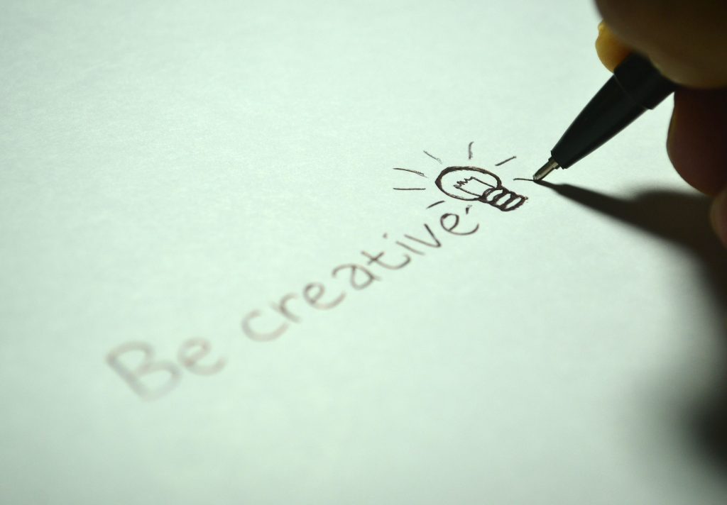 Close-up of handwritten 'Be creative' with a light bulb sketch on paper. Gros plan sur "Soyez créatif" écrit à la main avec un croquis d'ampoule sur papier.