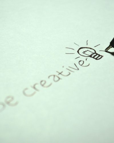 Close-up of handwritten 'Be creative' with a light bulb sketch on paper. Gros plan sur "Soyez créatif" écrit à la main avec un croquis d'ampoule sur papier.