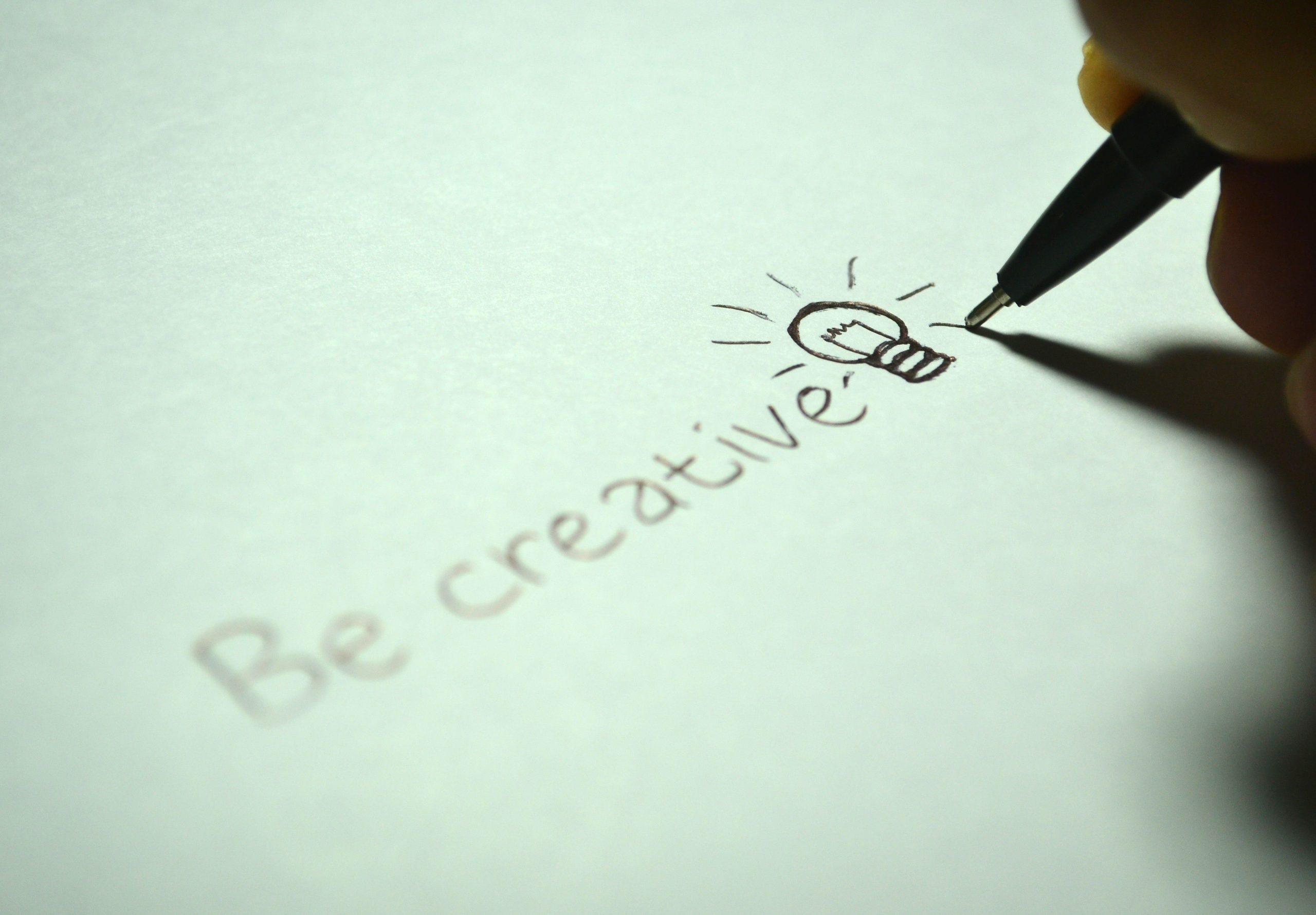 Close-up of handwritten 'Be creative' with a light bulb sketch on paper. Gros plan sur "Soyez créatif" écrit à la main avec un croquis d'ampoule sur papier.