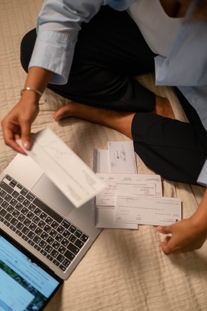 An adult organizing cheques and using a laptop indoors for financial tasks. Un adulte organisant des chèques et utilisant un ordinateur portable à l'intérieur pour des tâches financières.