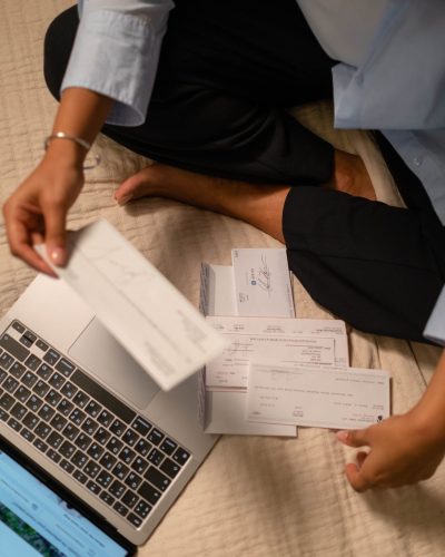 An adult organizing cheques and using a laptop indoors for financial tasks. Un adulte organisant des chèques et utilisant un ordinateur portable à l'intérieur pour des tâches financières.