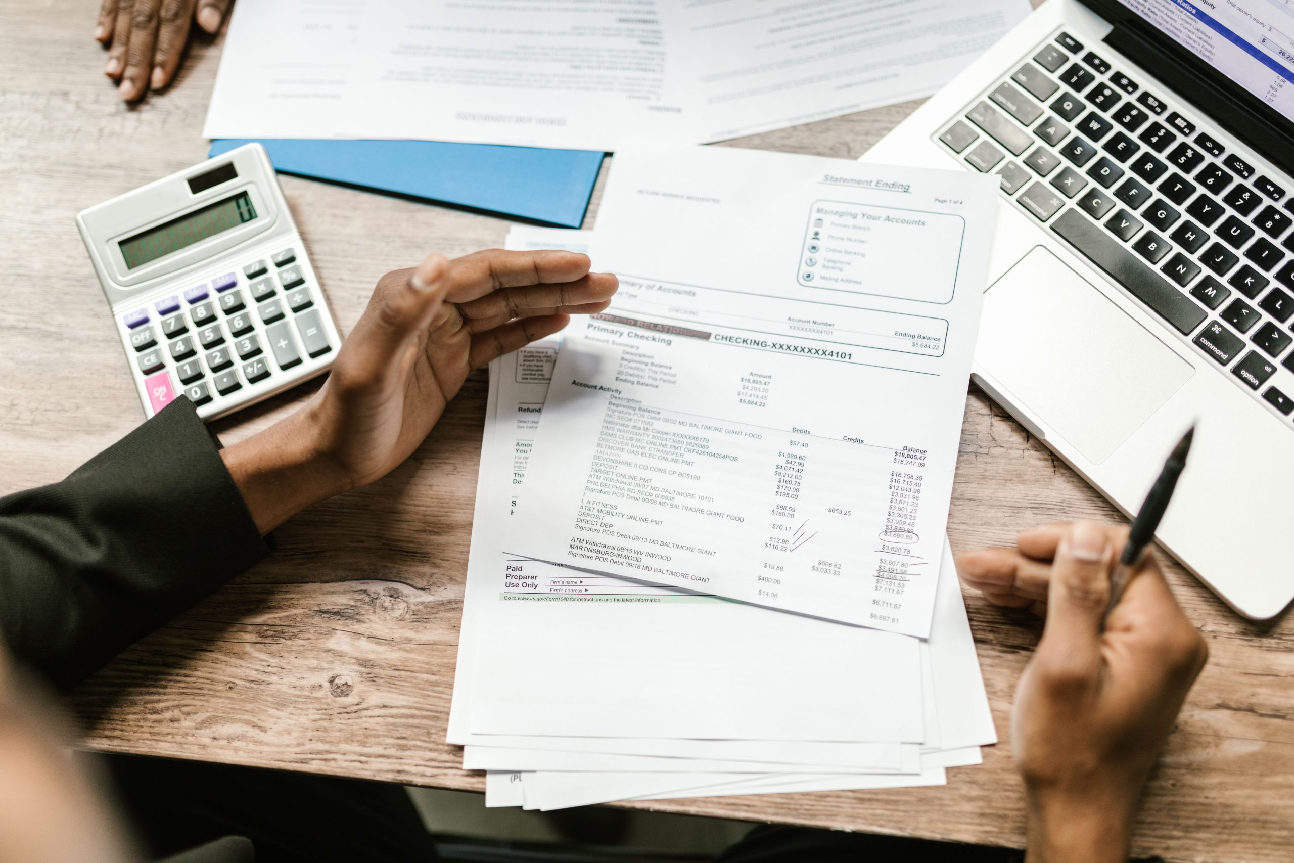 Hands holding financial documents with calculator and laptop on office desk, business analysis scene. Des mains tenant des documents financiers avec calculatrice et ordinateur portable sur un bureau de bureau, scène d'analyse commerciale.